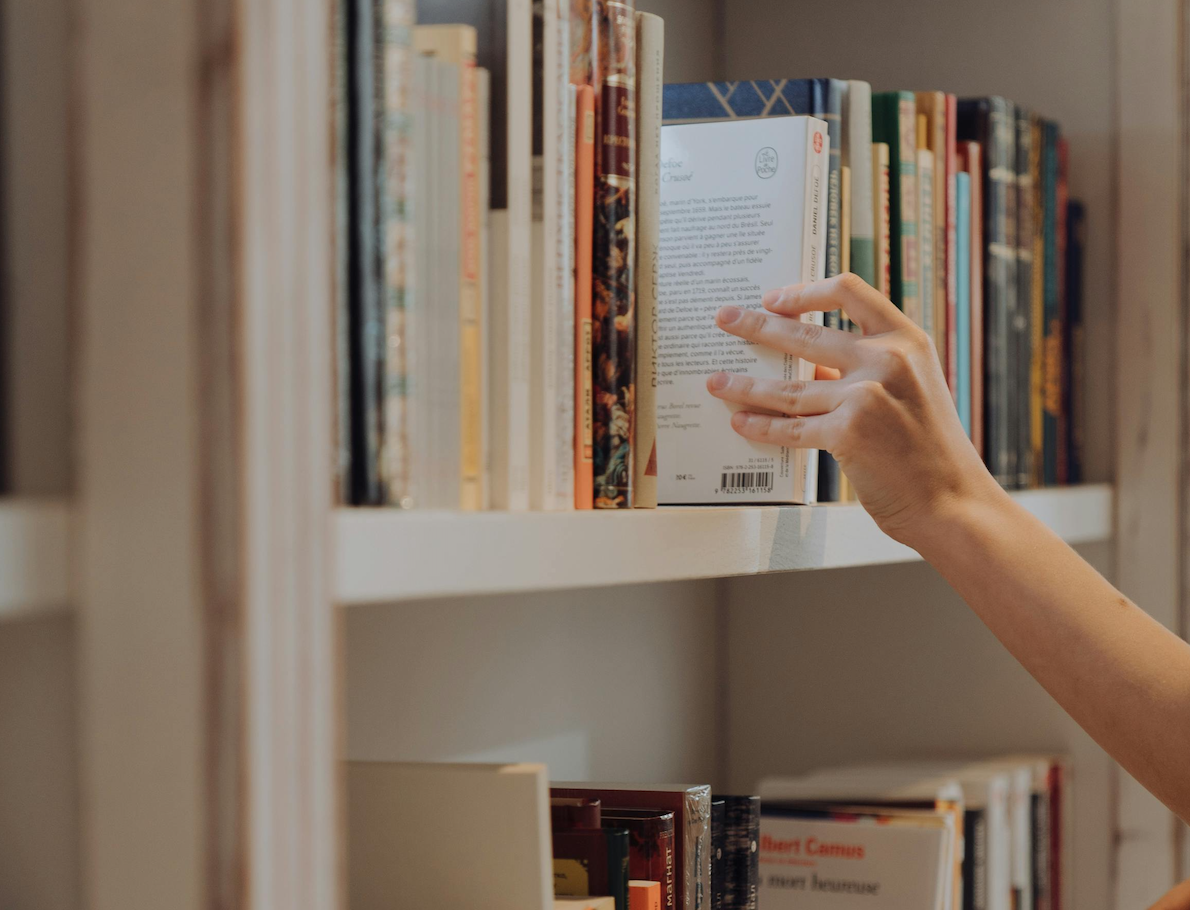 Main qui sélectionne un livre dans une bibliothèque, symbole de la mémoire de ChatGPT et de la personnalisation de l'information